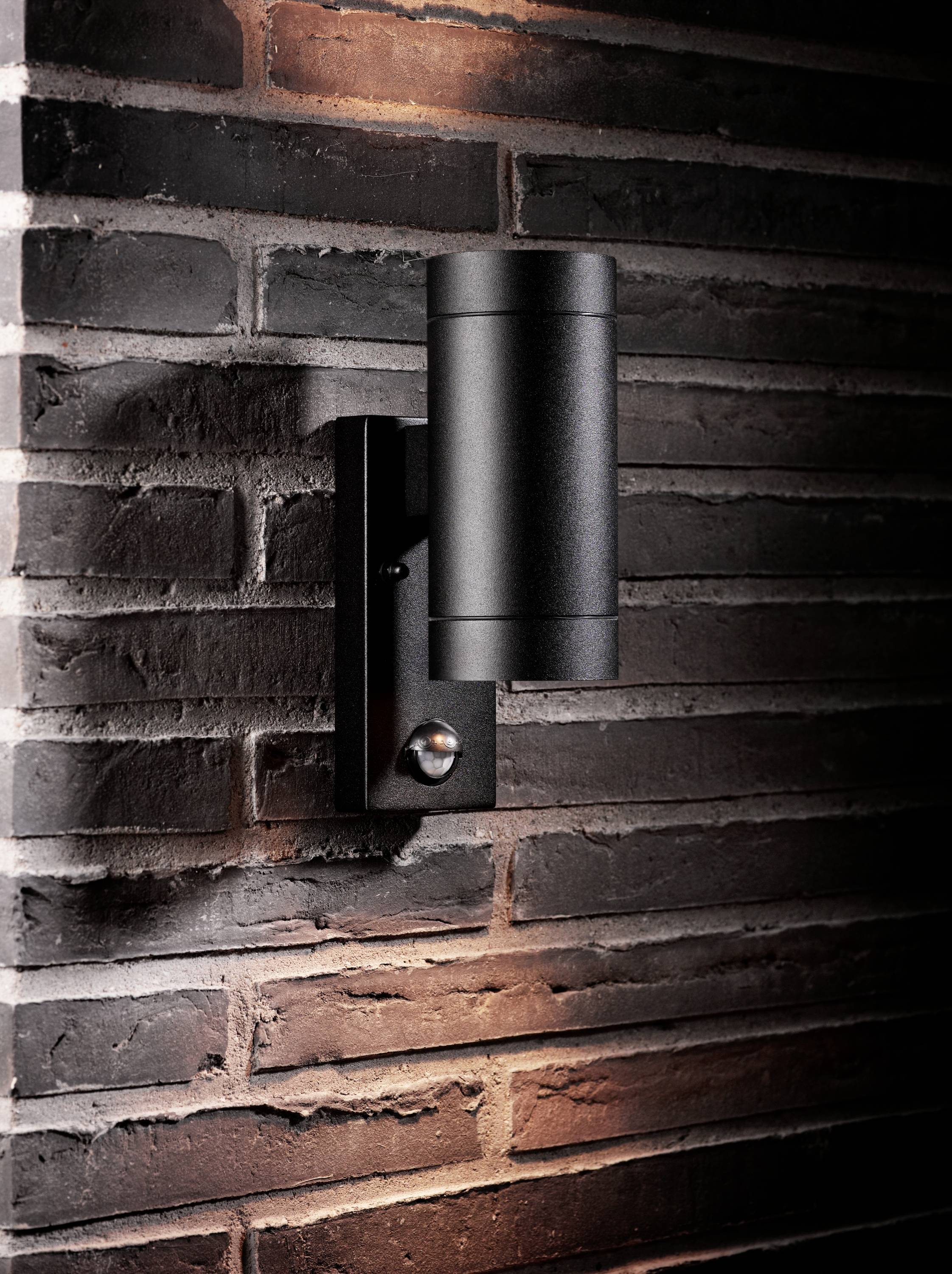 Zwarte wandlamp van metaal gemonteerd aan een bakstenen muur, verlicht van boven en beneden, biedt decoratieve buitenverlichting.