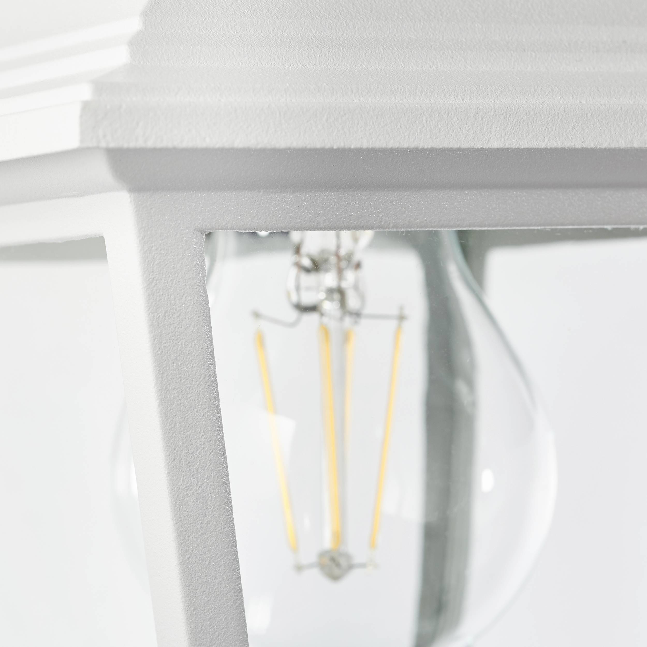 Een lamp met een heldere gloeilamp in een wit lampenkap, verlicht door natuurlijk licht.