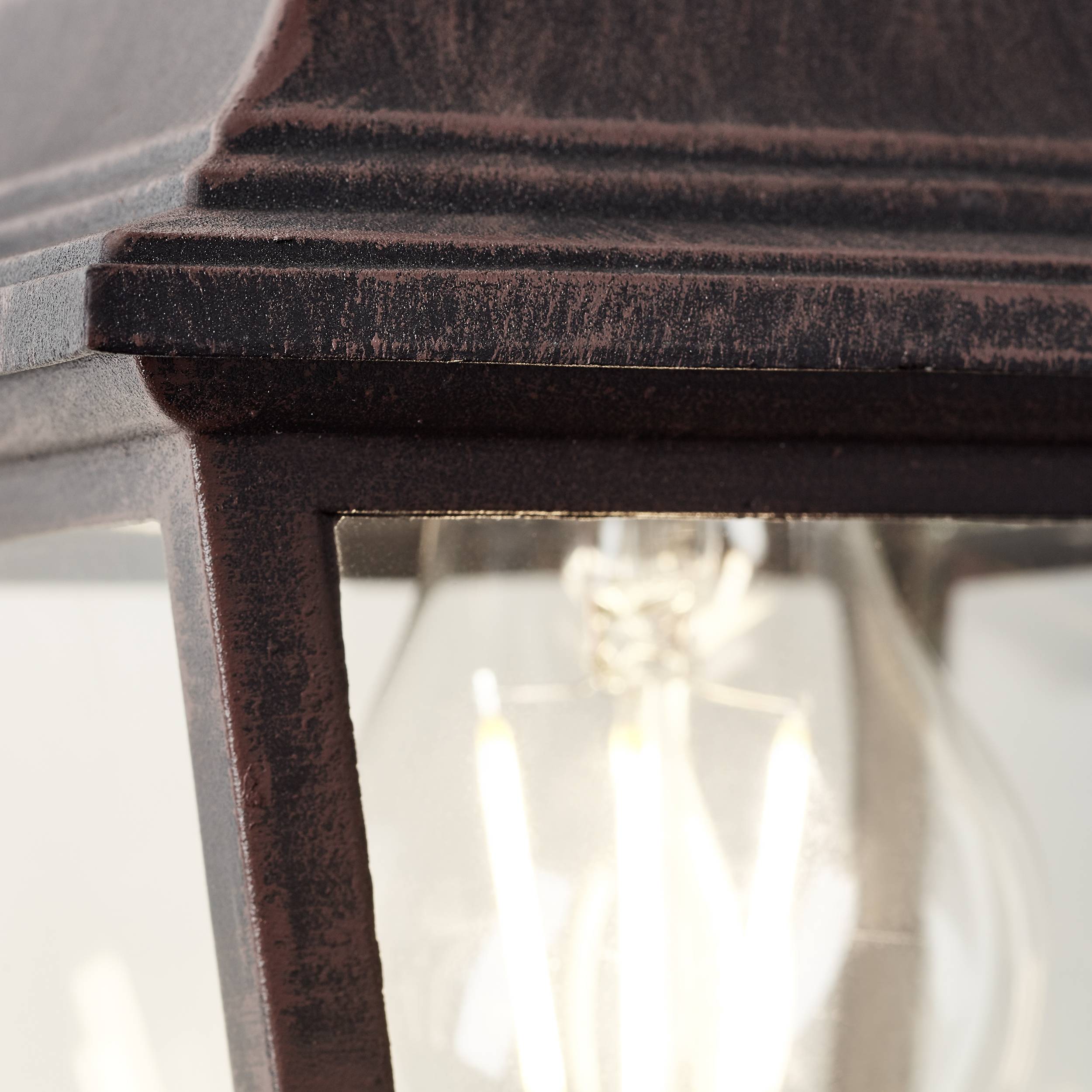 Close-up van een antieke lantaarn met zichtbare gloeilamp die warm licht uitstraalt. Rustieke, metalen oppervlak van de lantaarn.
