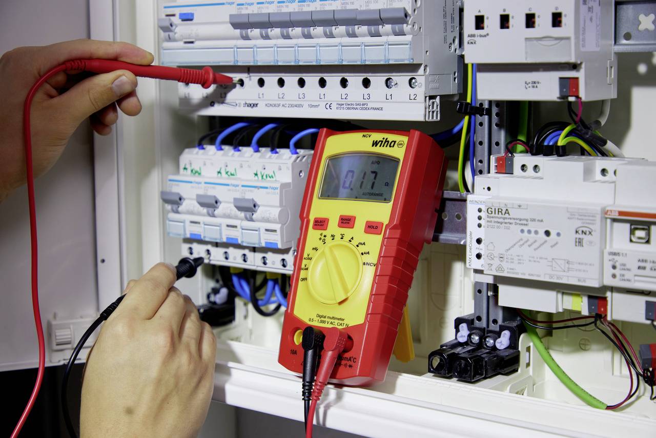 Een persoon meet met een multimeter de spanning in een zekeringkast om elektrische waarden te controleren.