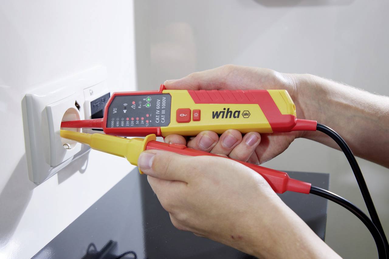 Een persoon meet met een spanningzoeker de spanning van een stopcontact. De tester toont een meetresultaat op het display.