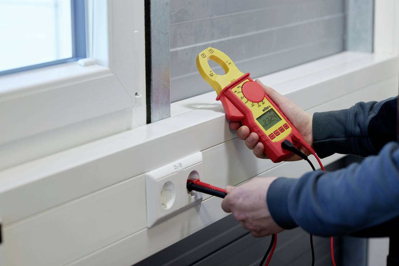 Een persoon meet de spanning op een stopcontact met een digitale multimeter.