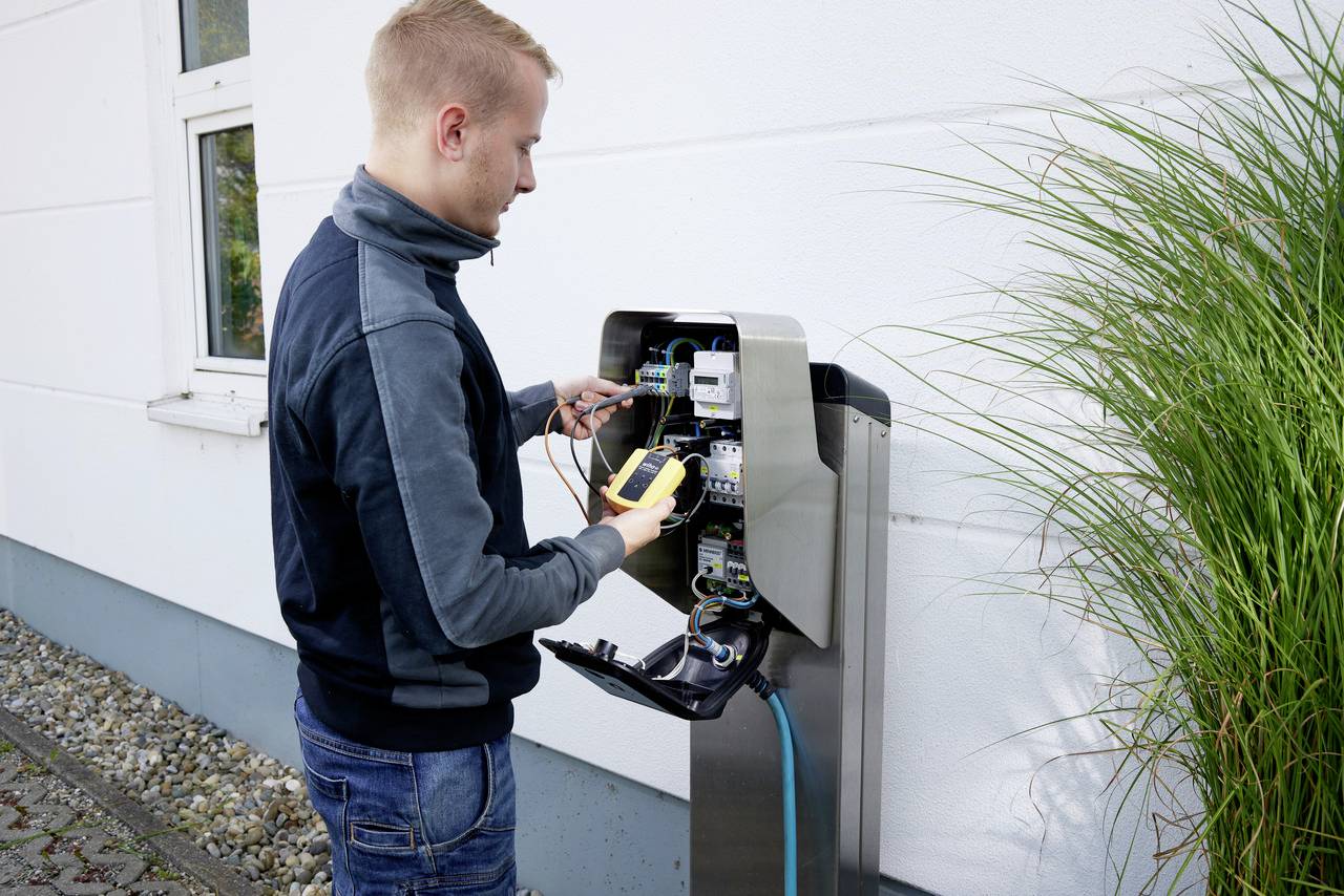 Een man controleert een elektrisch laadstation met een multimeter.