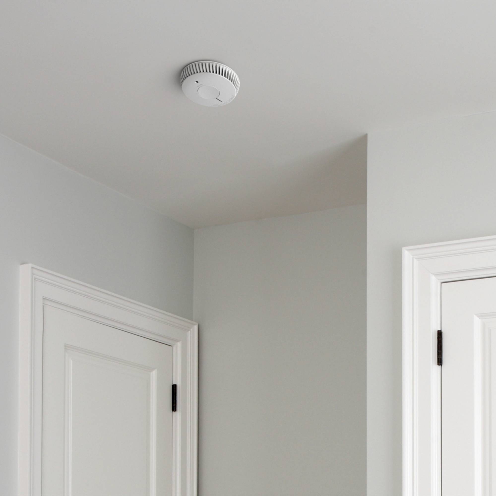 Een rookmelder is aan het plafond van een ruimte naast een deur gemonteerd om de veiligheid in het gebouw te verhogen.