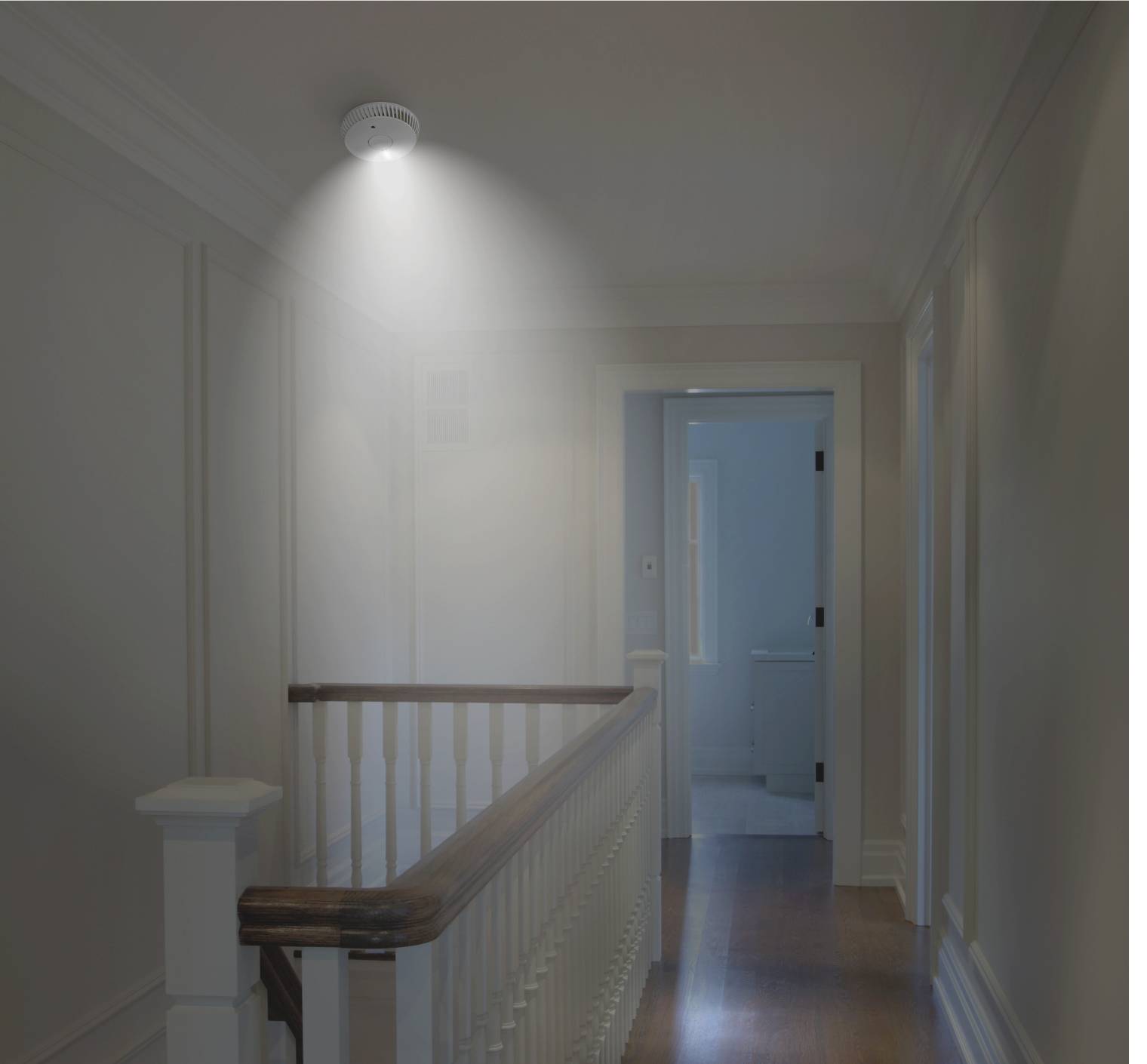 Een verlichte gang met een rookmelder aan het plafond. Achter de gang bevindt zich een openstaande deur die naar een badkamer leidt.