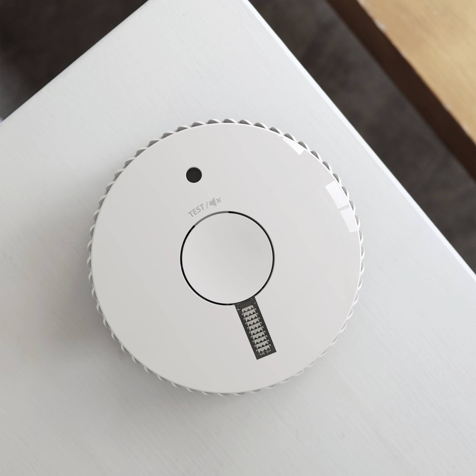 Een ronde rookmelder aan een witte plafond. Hij heeft een grote knop in het midden met de tekst 'TEST'.