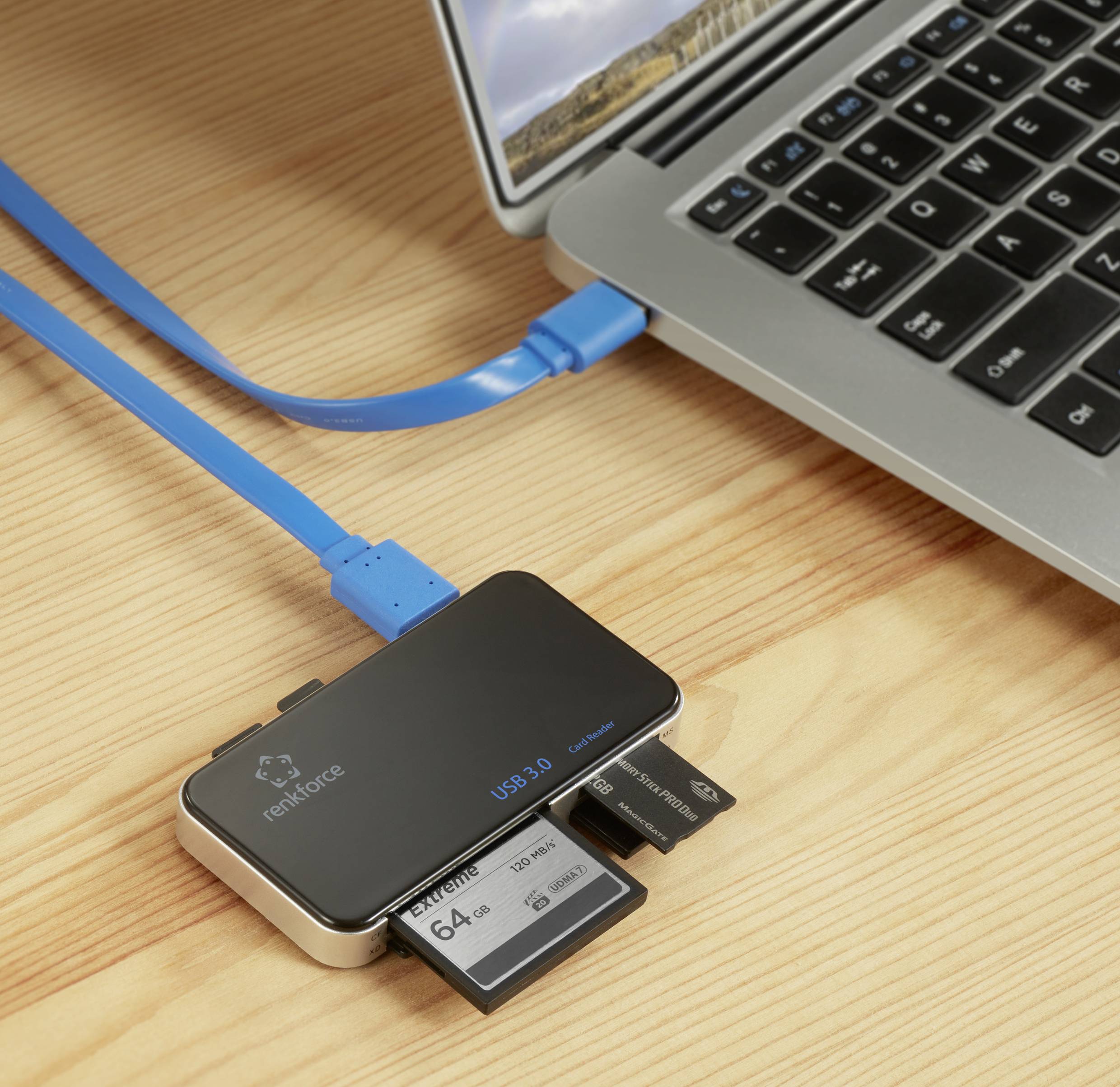 Een USB-hub met drie gestoken geheugenkaarten is via een blauw kabel verbonden met een laptop op een houten tafel.