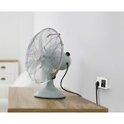 Een tafelventilator op een houten tafel is aangesloten op een slimme stopcontact dat gegevens over energieverbruik weergeeft.