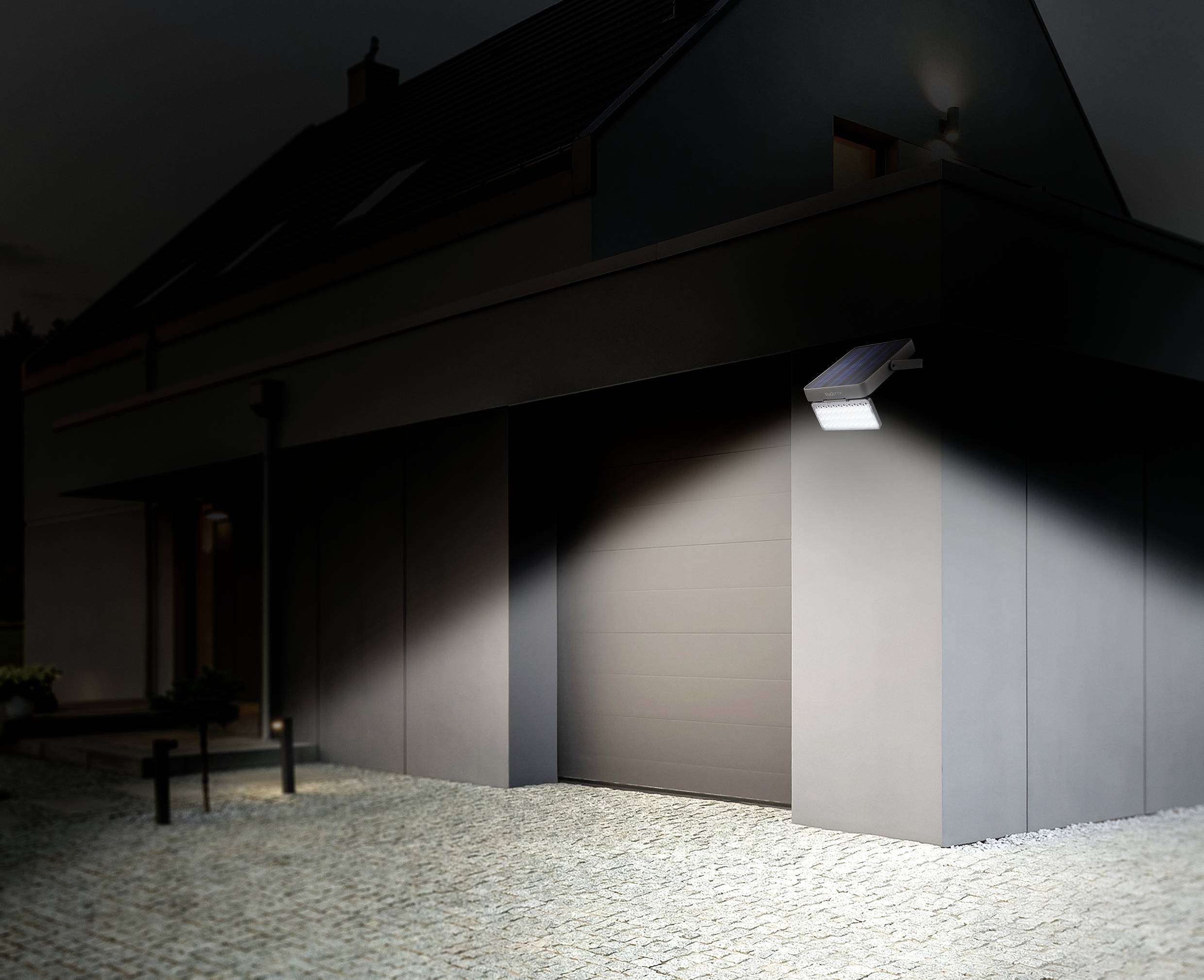 Een modern huis 's nachts met een ingeschakelde bewegingssensor-schijnwerper die de oprit verlicht.