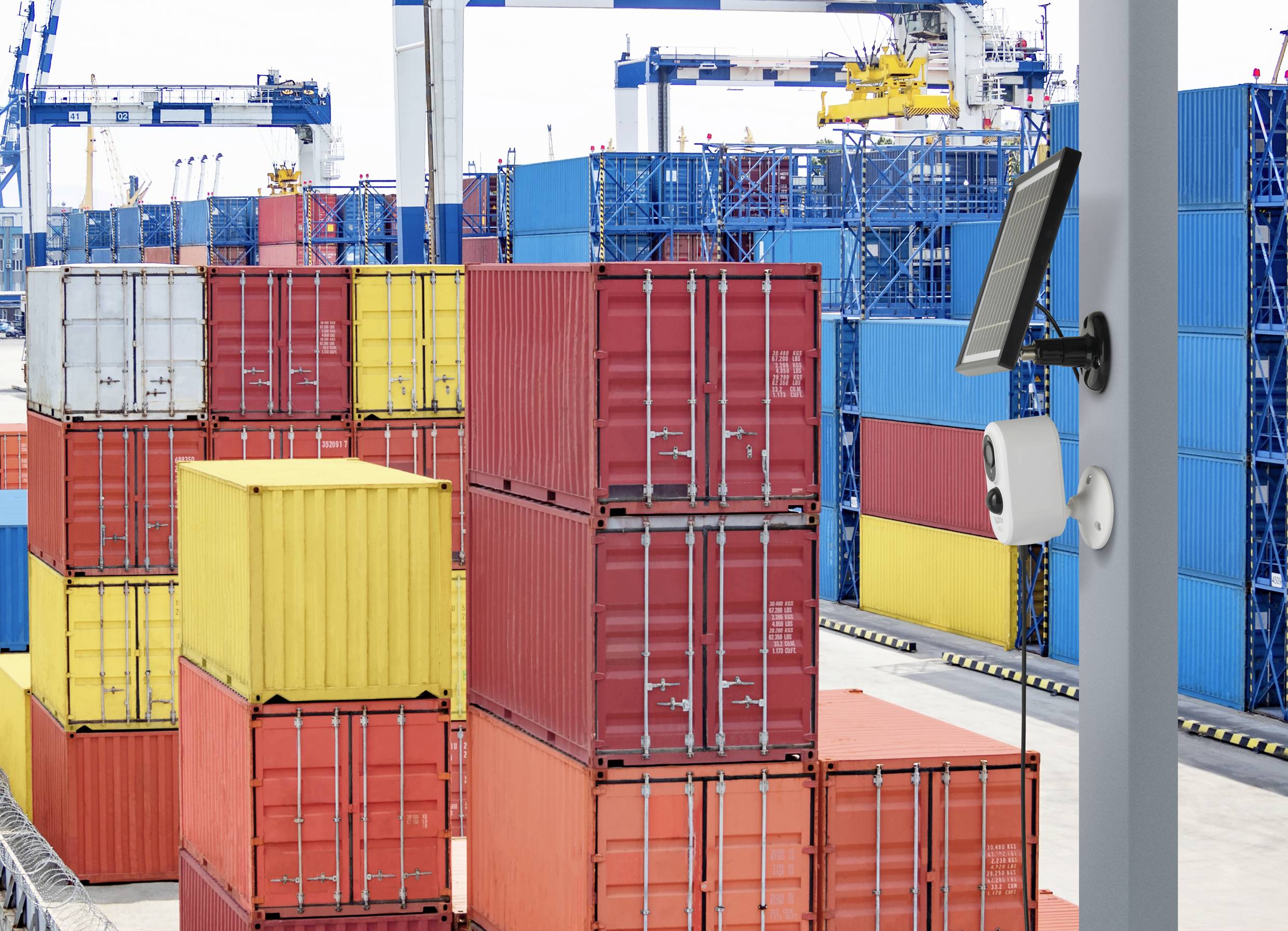 Containerhaven met gestapelde, kleurrijke vrachtcontainers en een bewakingssysteem op de voorgrond. Kranen op de achtergrond.