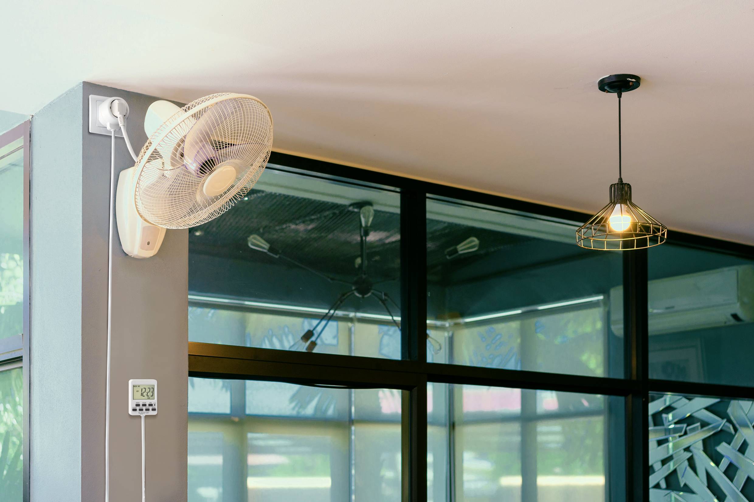 Een aan de muur gemonteerde ventilator en een hangende lamp in een moderne binnenruimte met grote ramen en veel daglicht.