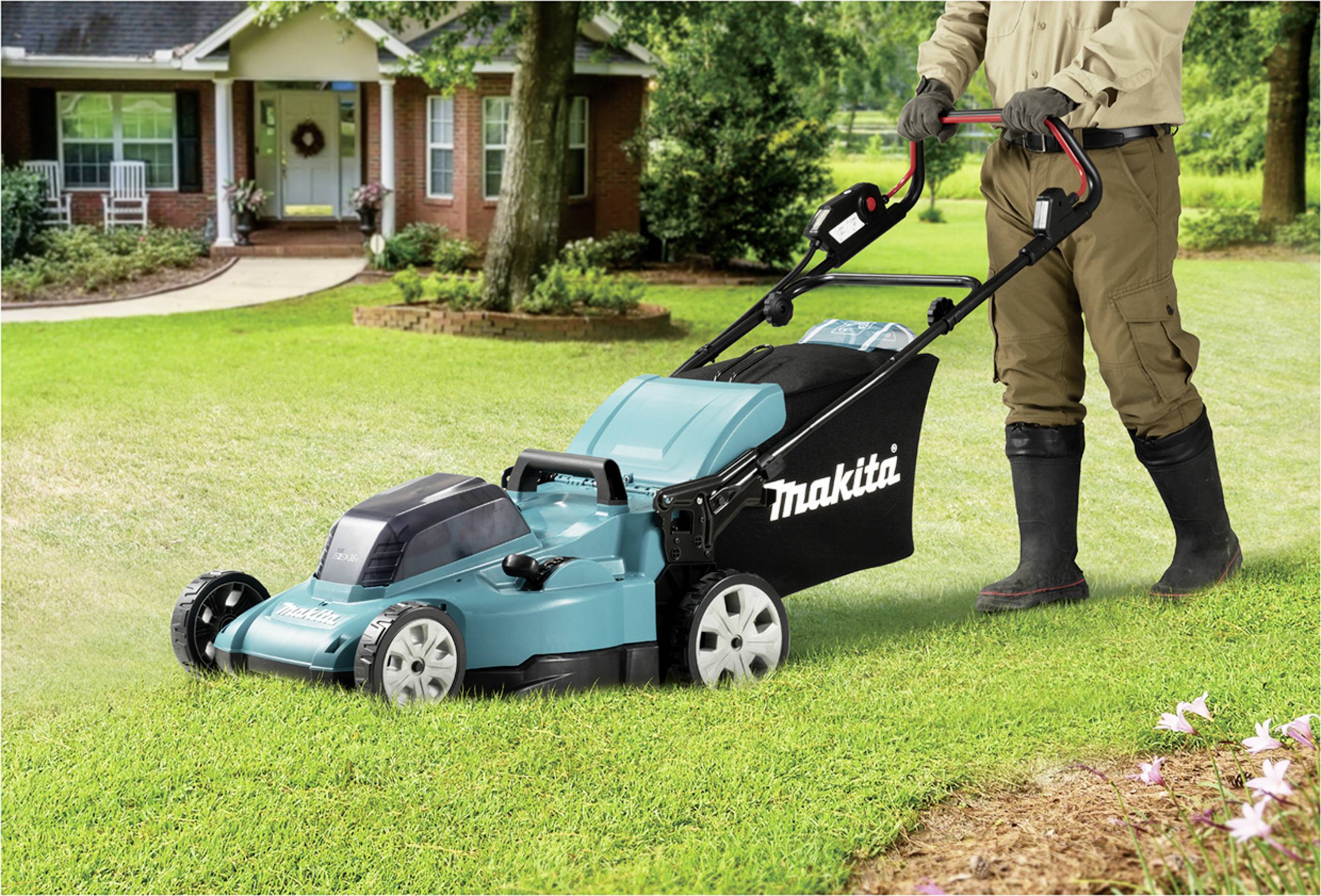 Een persoon maait het gazon met een turquoise grasmaaier in een tuin voor een huis.