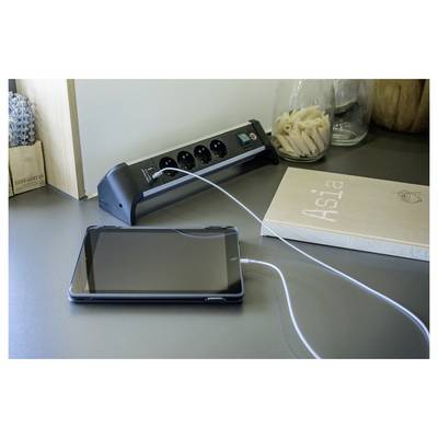 Tablet oplaadt op een bureau naast een stekkerdoos en een boek getiteld 'Aisla'.