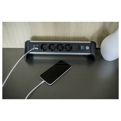 Een smartphone die op een bureau oplaadt naast een stekkerdoos met meerdere stopcontacten en een lamp.