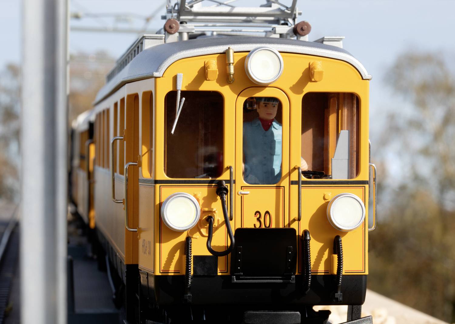 Een gele trein met nummer 30 rijdt op een route. Vooraan is een bestuurderscabine zichtbaar met daarin een persoon.