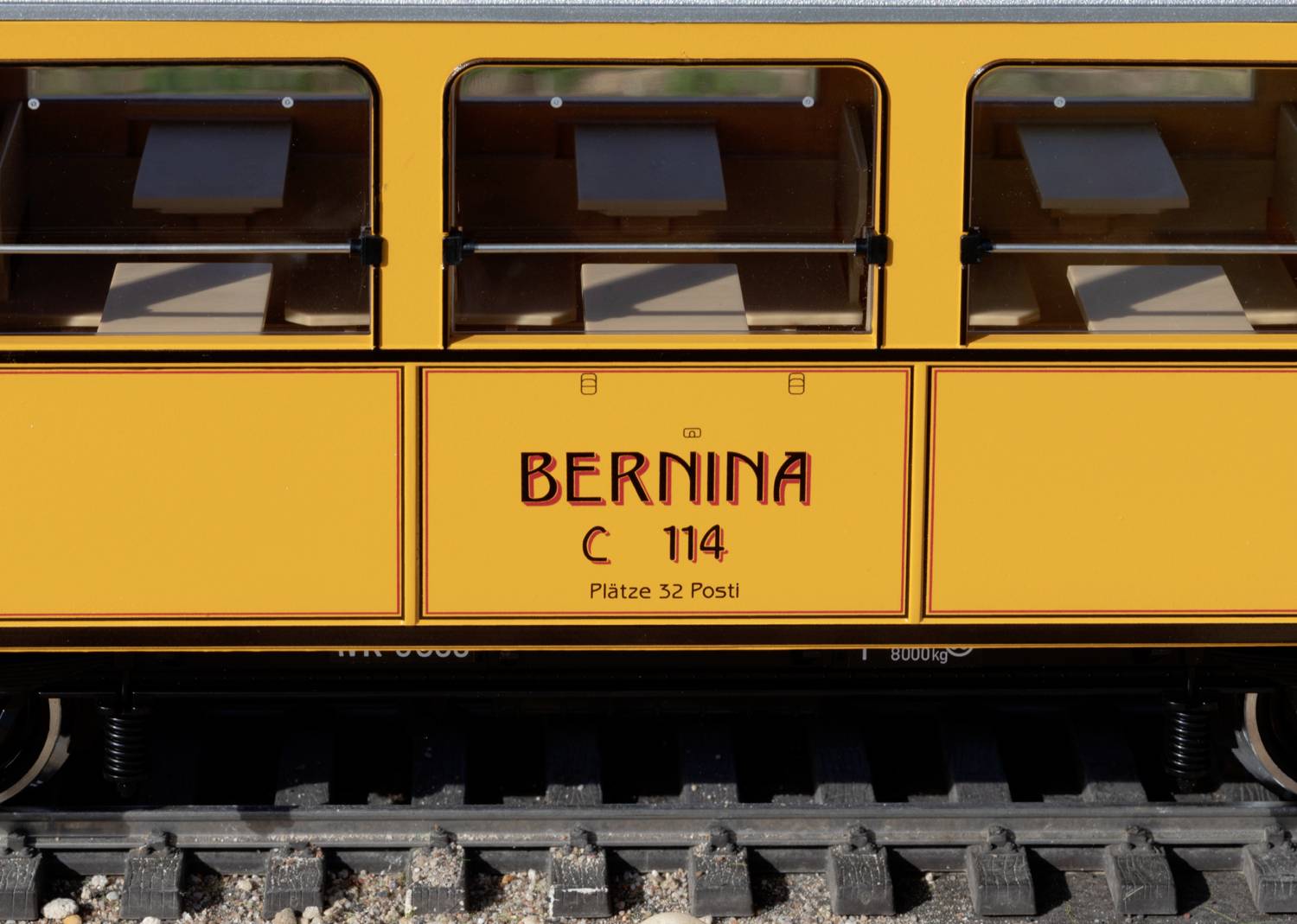 Een gele spoorwagon met het opschrift 'Bernina C 114, Plaatsen 32 Posti'. De wagon staat op spoorrails.