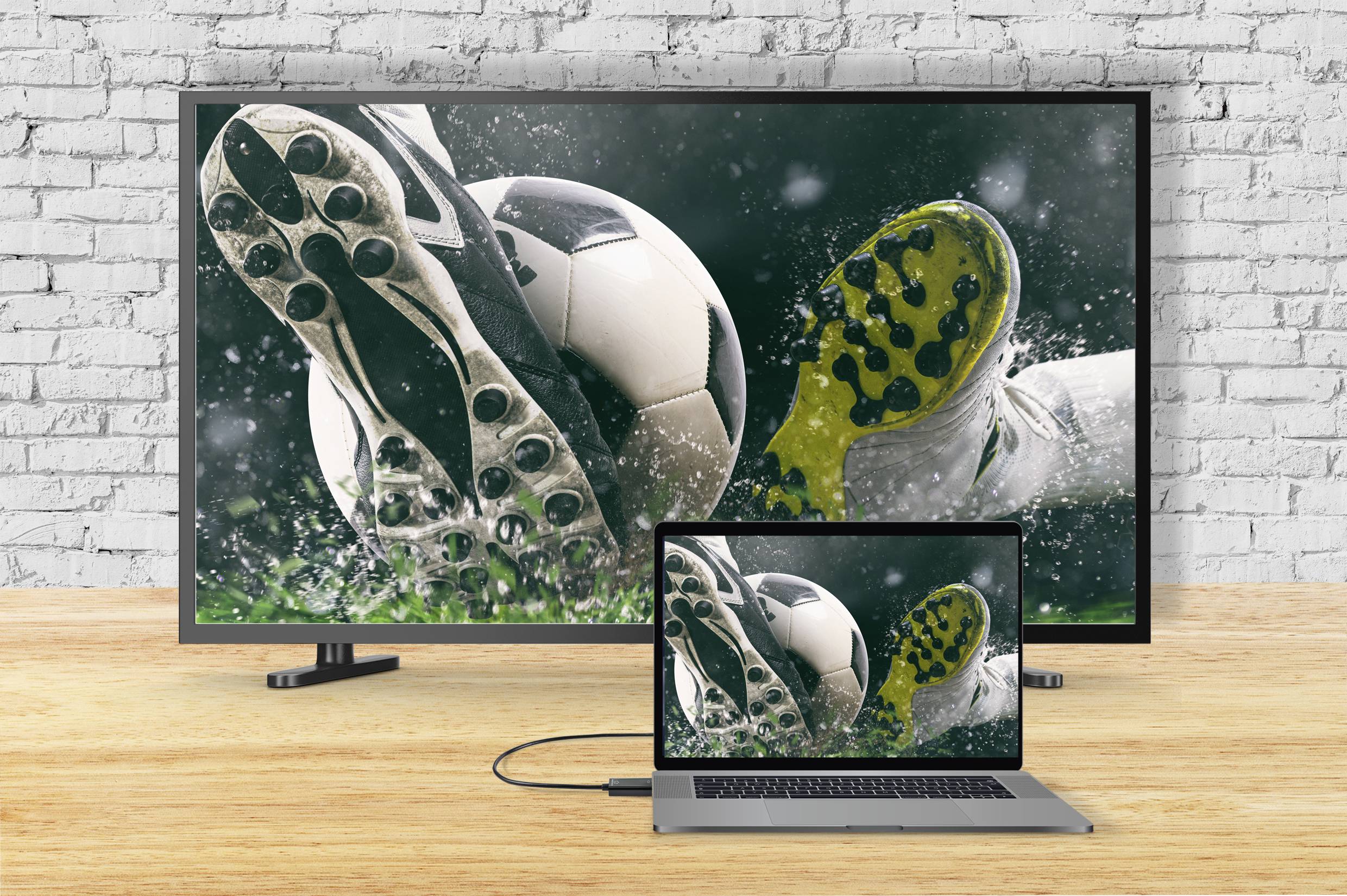 Een televisie en een laptop vertonen hetzelfde beeld: voetbalschoenen in actie die een natte bal trappen.