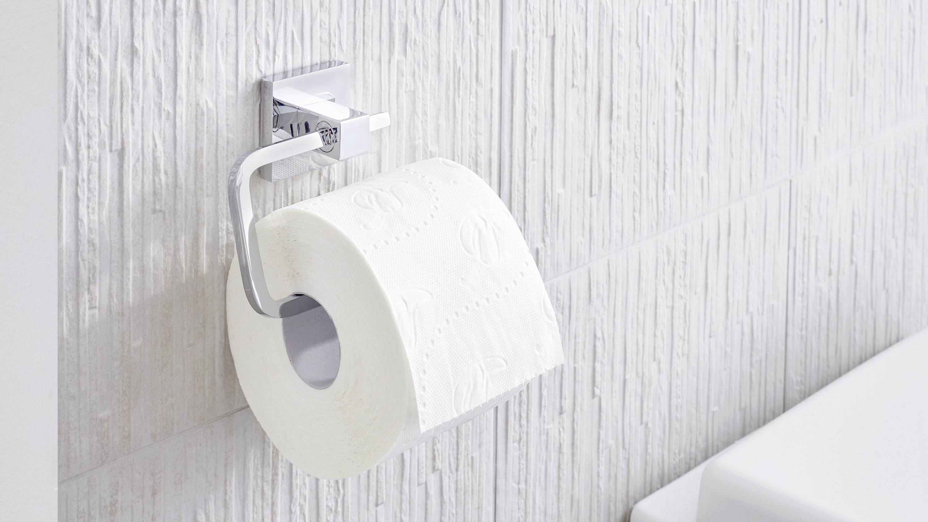 Wc-rol hangt aan een verchroomde houder tegen een gestructureerde witte badkamermuur.