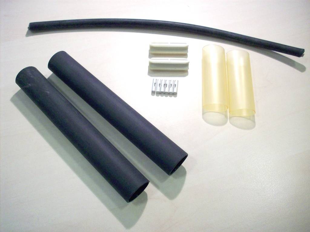 Zwarte en gele krimpkousen, metalen contacten en kunststof bevestigingen liggen op een witte ondergrond. Elektrotechnisch installatiemateriaal.
