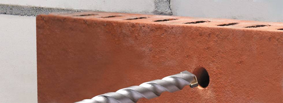 Een boor dringt in een rode baksteen door, om een gat te maken voor bevestigingen of installaties.