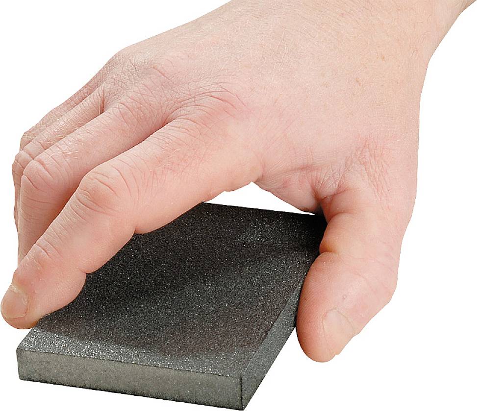 Een hand houdt een rechthoekige schuurblok met een donkere, korrelige oppervlakte.