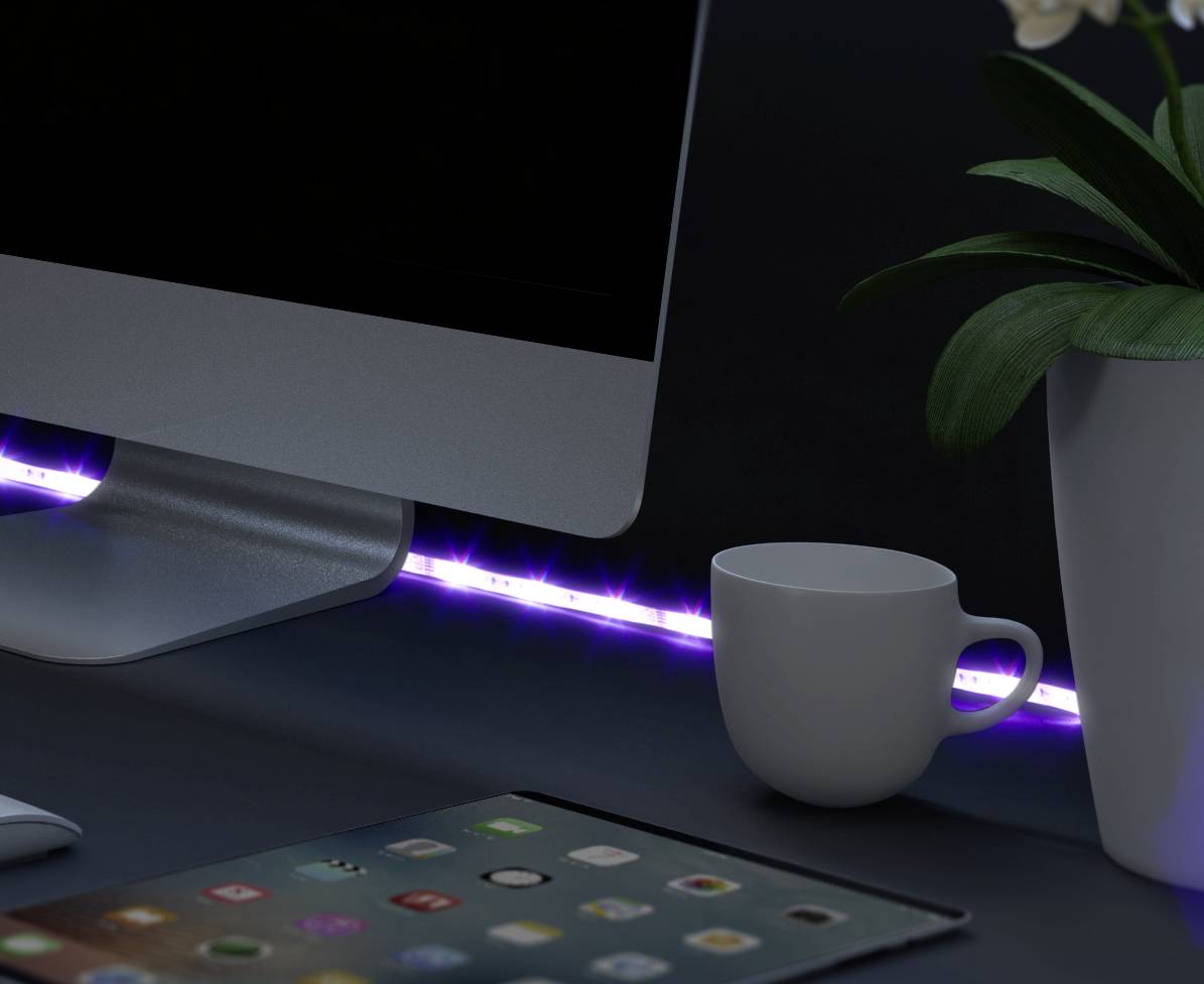 Een bureau met een computerscherm, een kopje, een plant in een pot en een tablet. LED-lichtsnoer op de achtergrond.