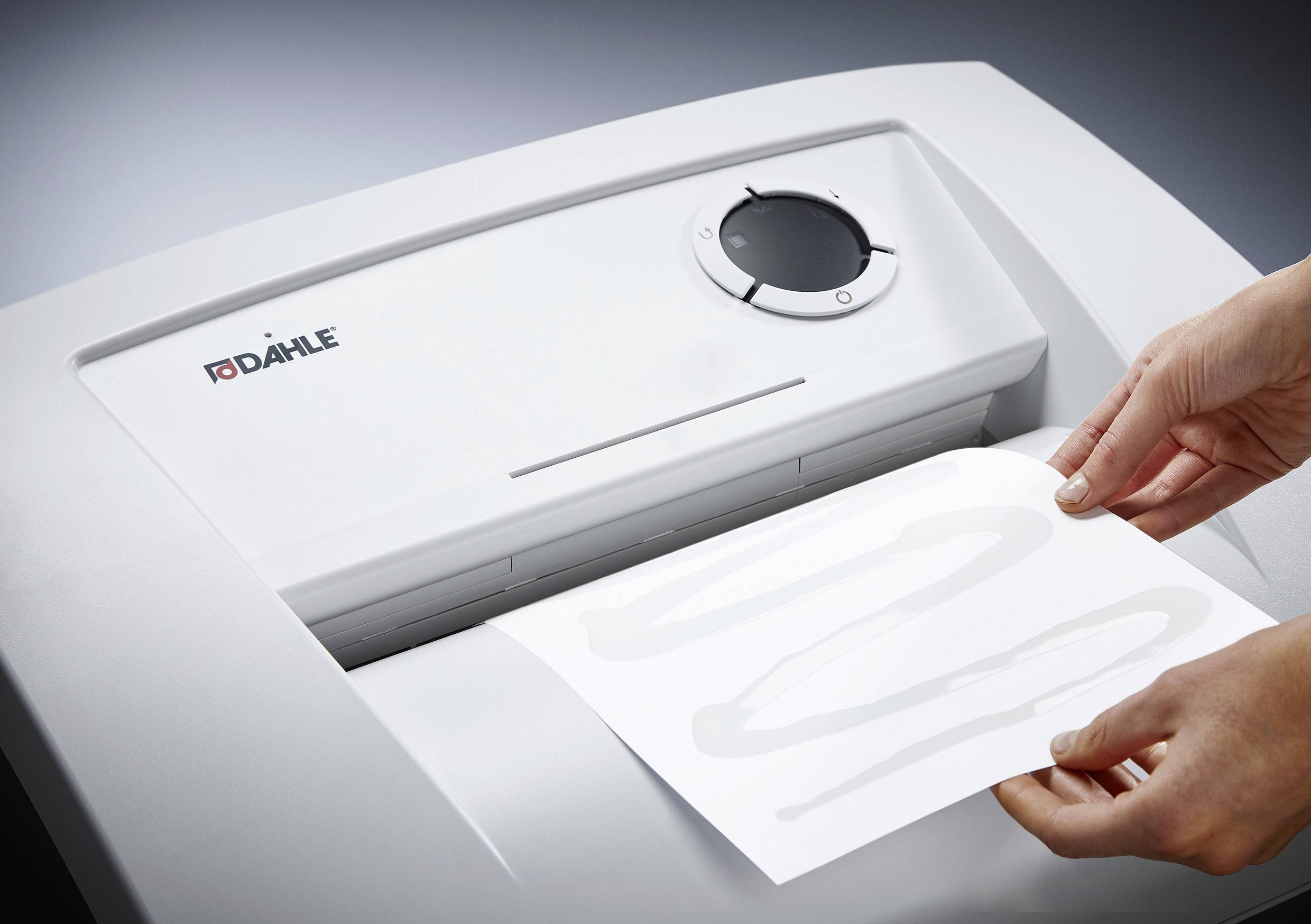 Iemand schuift een vel papier in een papierversnipperaar. Het apparaat heeft een witte oppervlakte en een bedieningspaneel met een draaiknop.