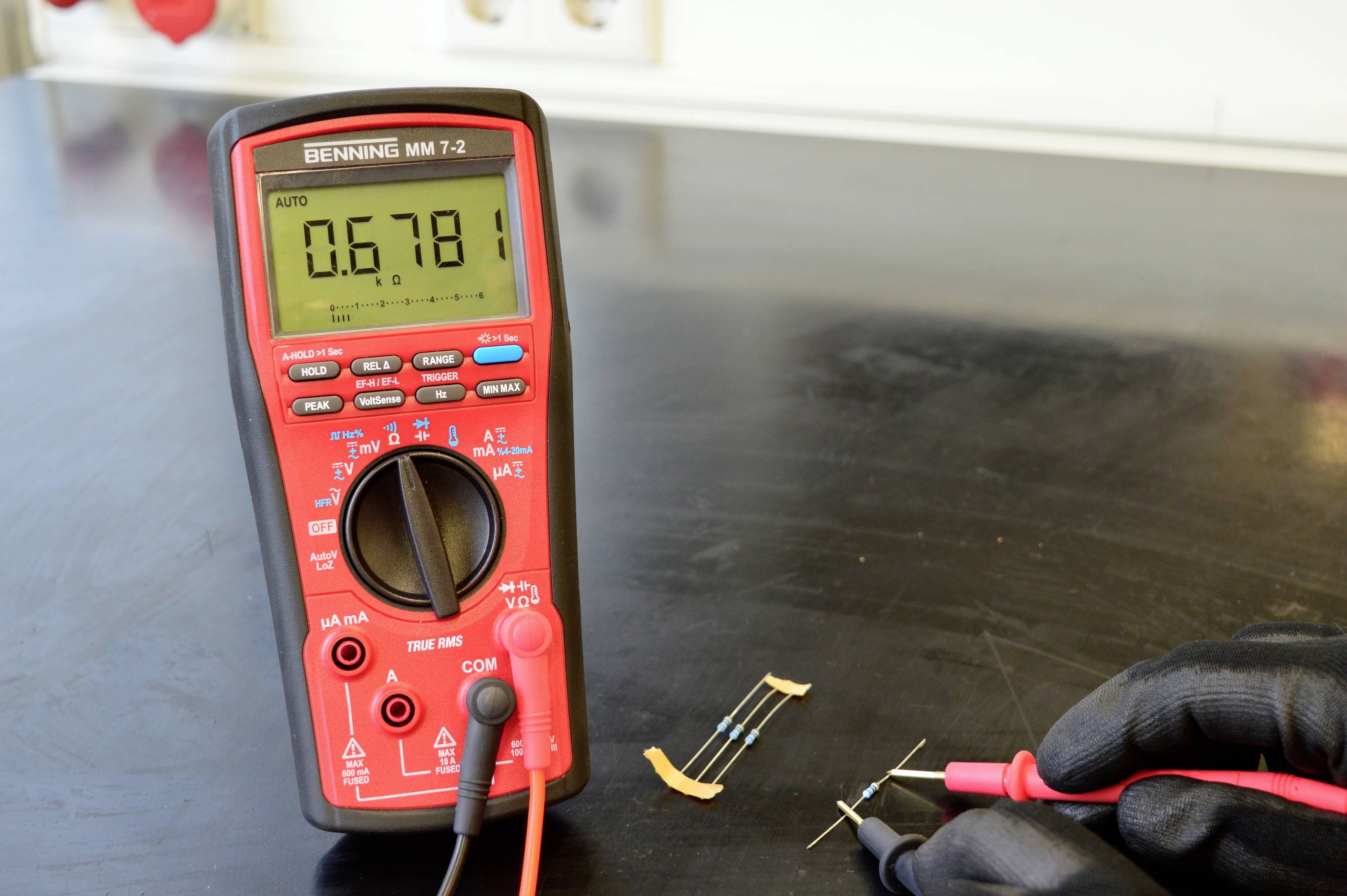 'Een multimeter meet de weerstand van een component dat op tafel ligt. Display toont waarde: 0,6781.'