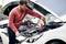 Een man in een rode trui geeft een auto starthulp met startkabels, motorkap geopend, op een parkeerplaats.