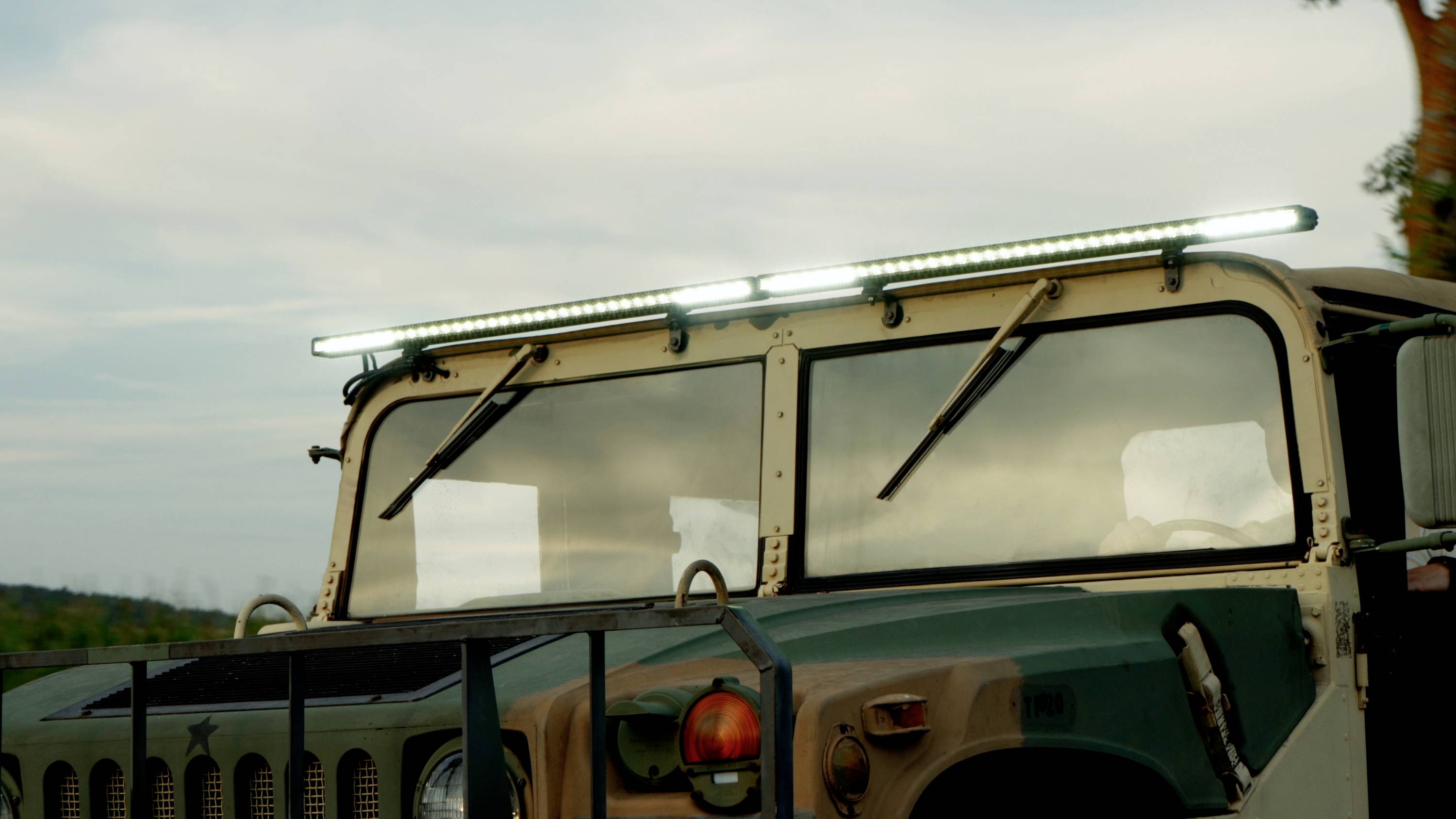 Een militair voertuig buiten, verlicht door LED-lampen op het dak, tegen een bewolkte hemel.