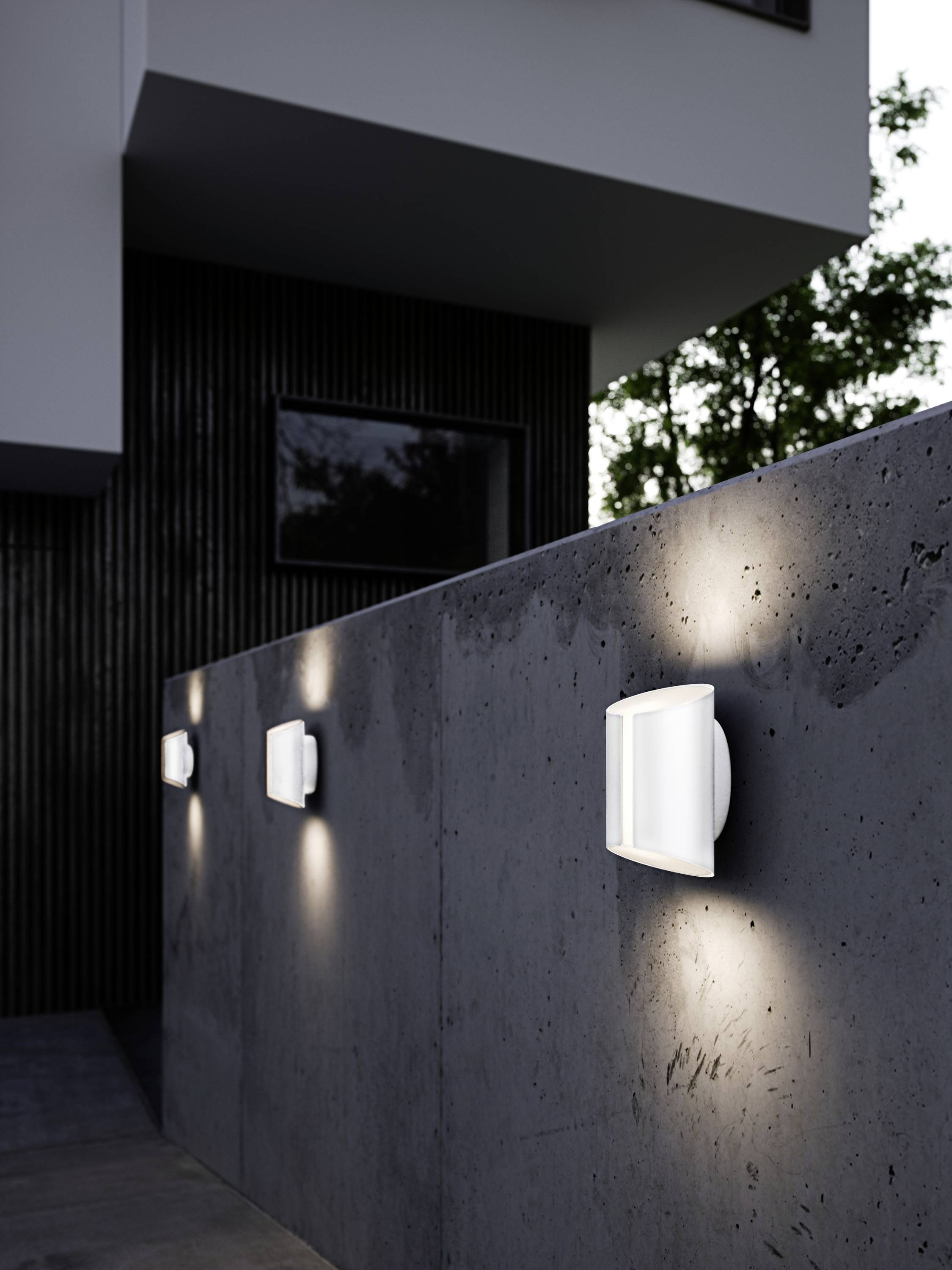 Moderne wandlampen verlichten een grijze betonnen muur voor een gebouw 's avonds.