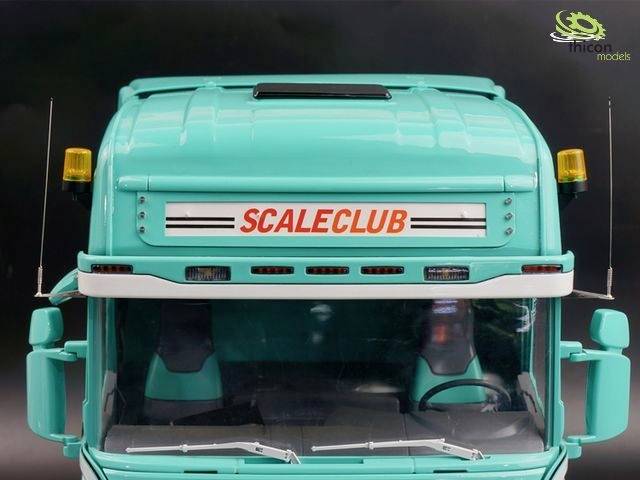 Turquoise vrachtwagenkop van voren met 'Scaleclub'-opschrift boven de voorruit. Gele waarschuwingslichten op het dak.