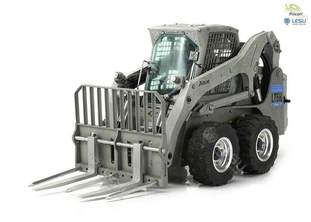 Een grijze compacte lader met vorkenframe, geschikt voor bouw- of landbouwwerkzaamheden. Merkenlogo's zichtbaar rechtsboven.