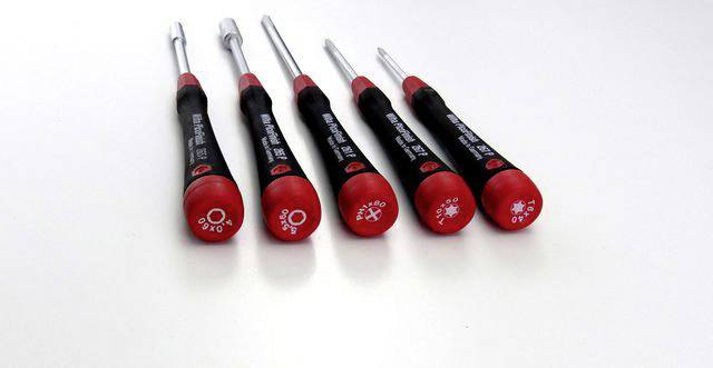 Vijf schroevendraaiers met rode handgrepen en verschillende symbolen liggen naast elkaar op een witte ondergrond.