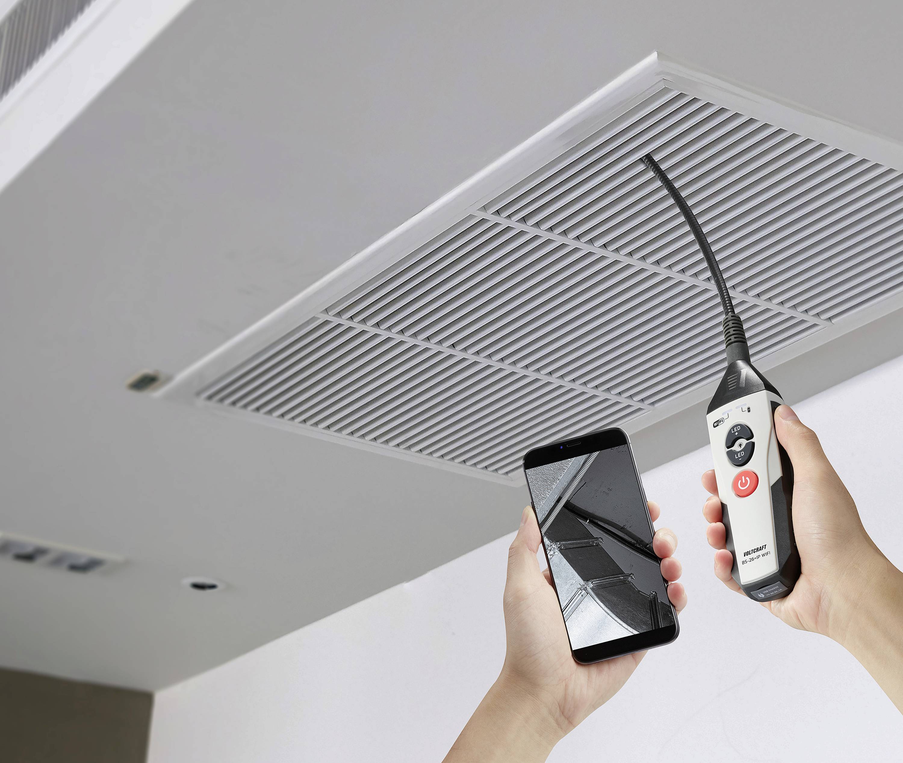 Een persoon inspecteert het binnenste van een ventilatieschacht aan het plafond met behulp van een endoscoopCamera en smartphone.