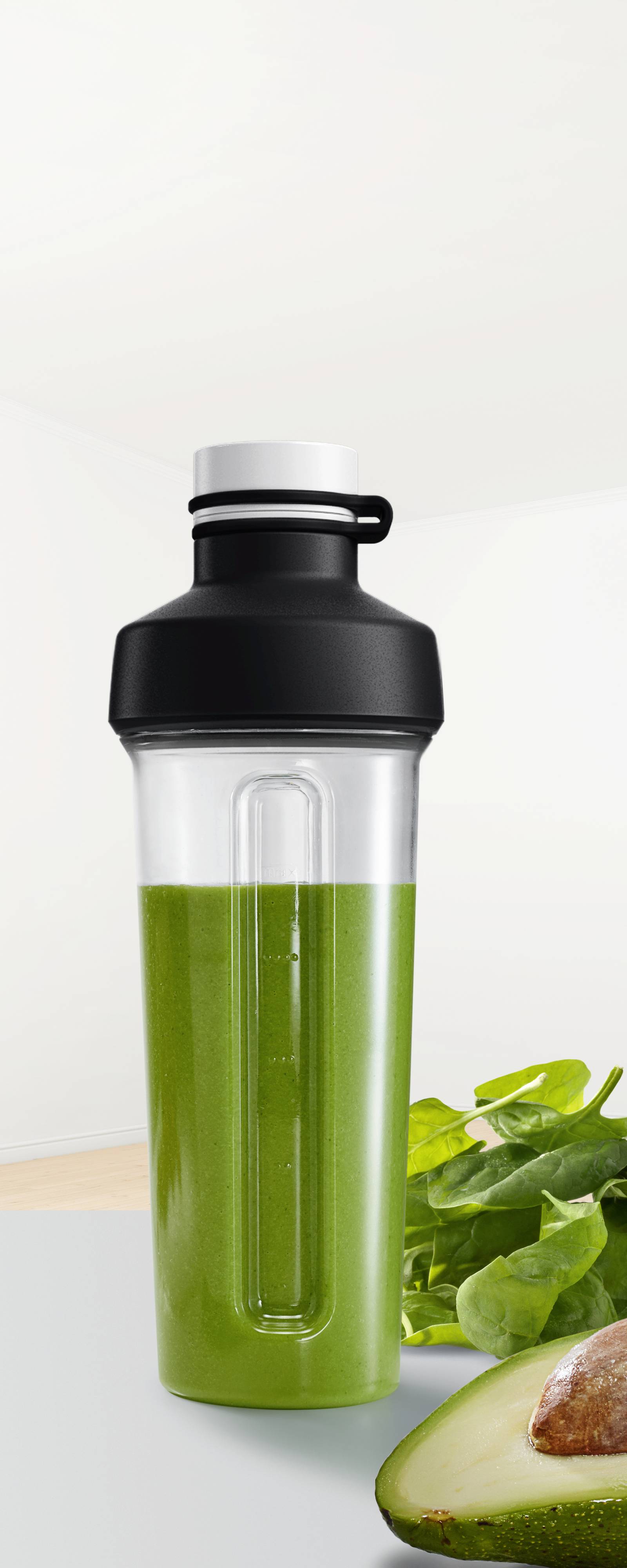 Een shaker met groene smoothie, naast een avocado en spinaziebladeren.