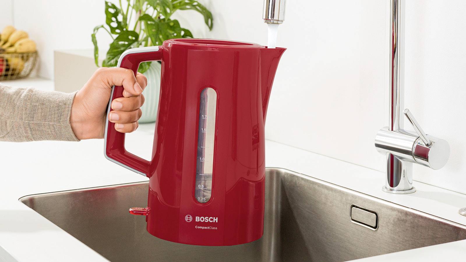 Een persoon vult een rode waterkoker van Bosch met water uit een kraantje in een keuken.