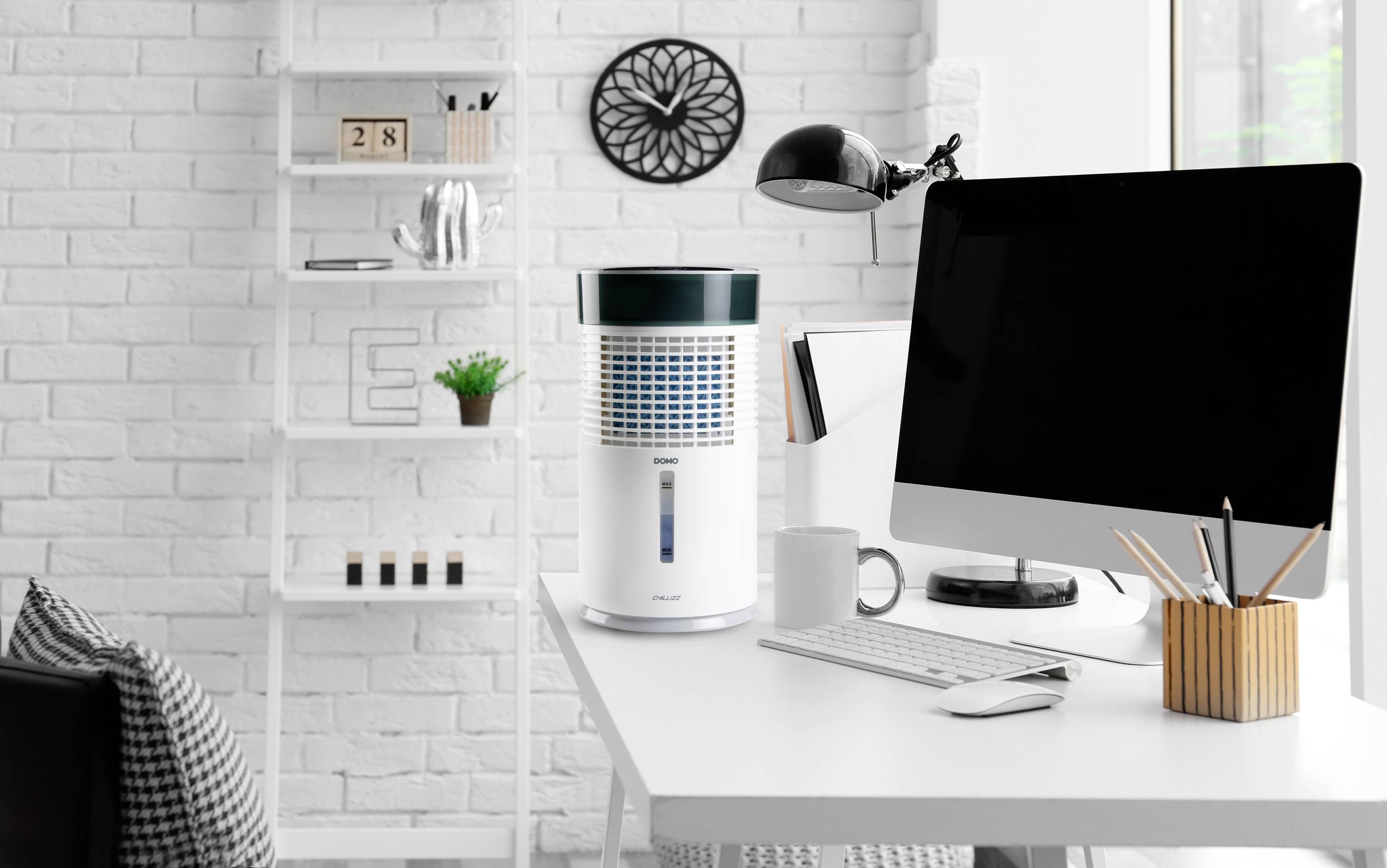 Een modern kantoor met een wit bureau waarop een computer, een lamp en een luchtreiniger staan. Op de achtergrond een boekenplank.