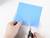 Een persoon knipt een blauw stuk papier met een schaar op een witte achtergrond.