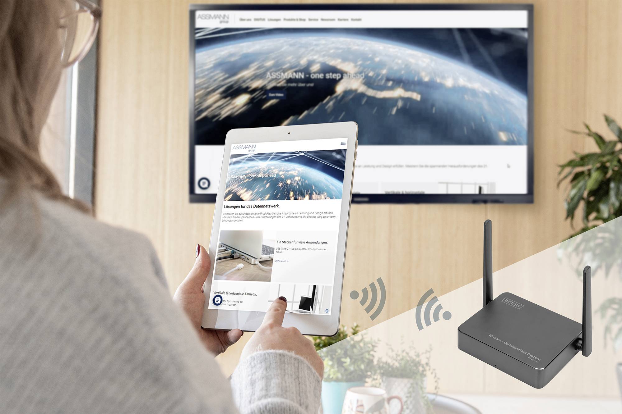 Een persoon bedient een tablet met een website die technische oplossingen toont. Op de achtergrond is een groot scherm zichtbaar.