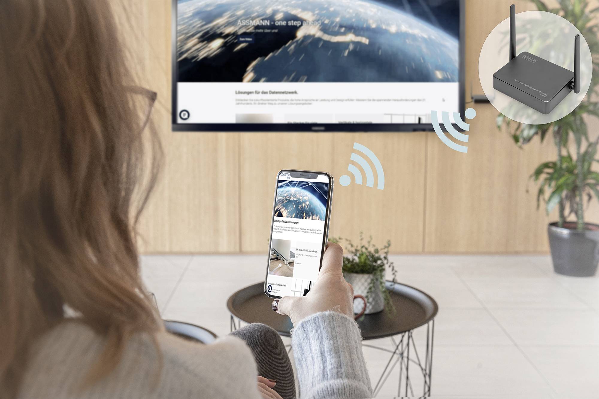 Een persoon bedient een Smart-TV met een smartphone, waarop een afbeelding van de ruimte wordt weergegeven. Een symbool toont de WLAN-verbinding met de router.