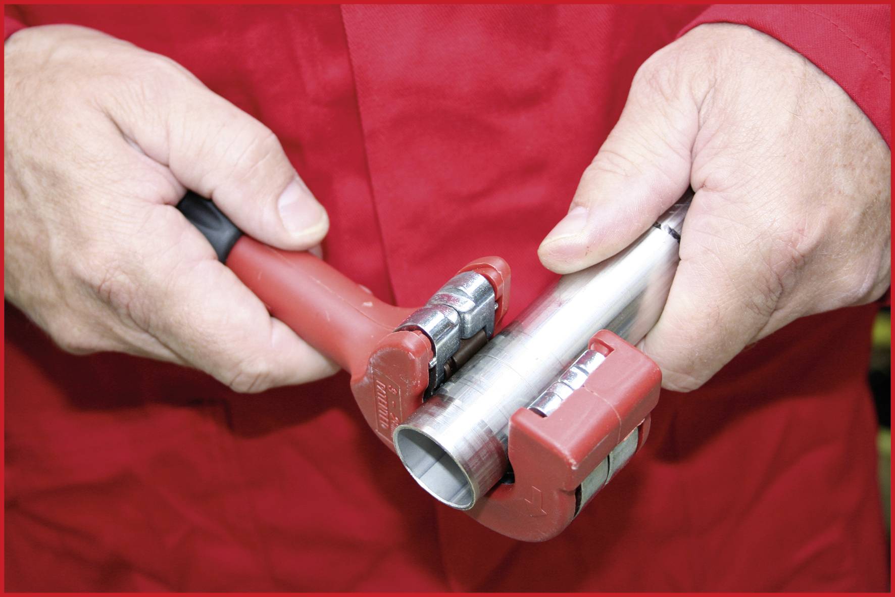 Een persoon gebruikt een rood gereedschap om een metalen buizensnijder aan te passen op een zilveren buis.