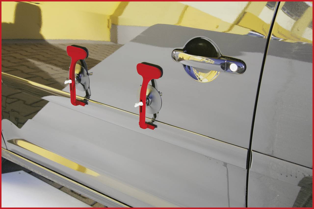 Twee rode zuignappen zijn bevestigd aan het glanzende oppervlak van een zilvergrijs voertuig, naast een zwarte deurkrukstrip.