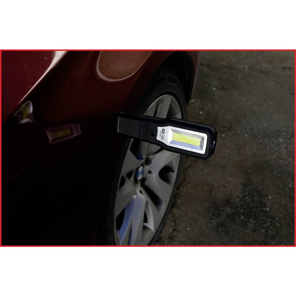 Een draagbare LED-lamp verlicht de band van een rode auto in een donkere omgeving om mogelijke bandschade te inspecteren.