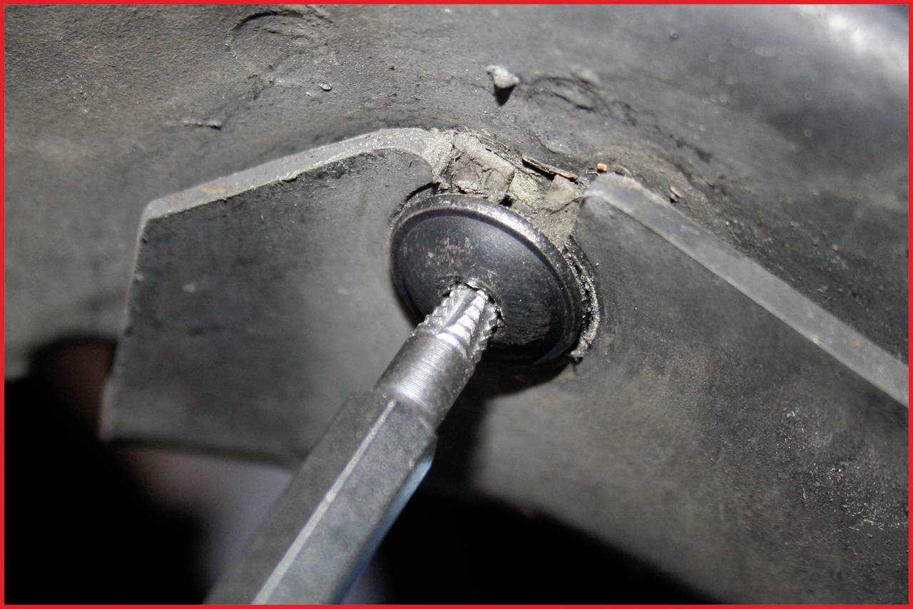 Close-up van een schroevendraaier die een schroef in een metalen onderdeel draait. Op de achtergrond is een ruwe oppervlakte zichtbaar.