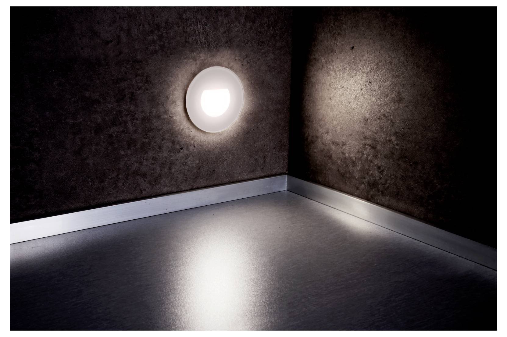 Leeg donker vertrek met een ronde wandlamp die een felle weerspiegeling op de vloer werpt.