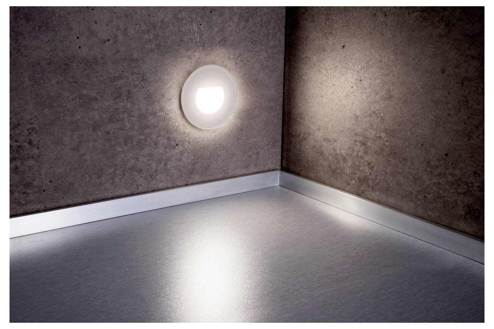 Lege hoekkamer met getextureerde grijze muren en vloer, verlicht door een enkele ronde wandlamp.