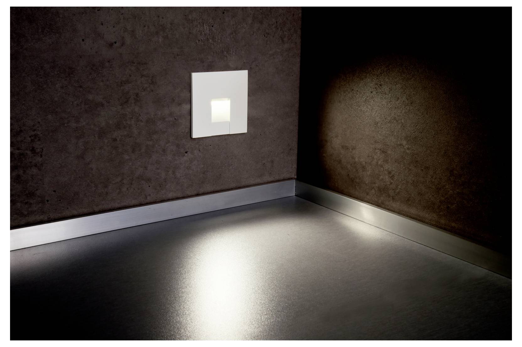 Lege donkere kamer met een klein vierkant lichtpaneel aan de muur dat een heldere weerspiegeling op de vloer en de hoekmuren werpt.
