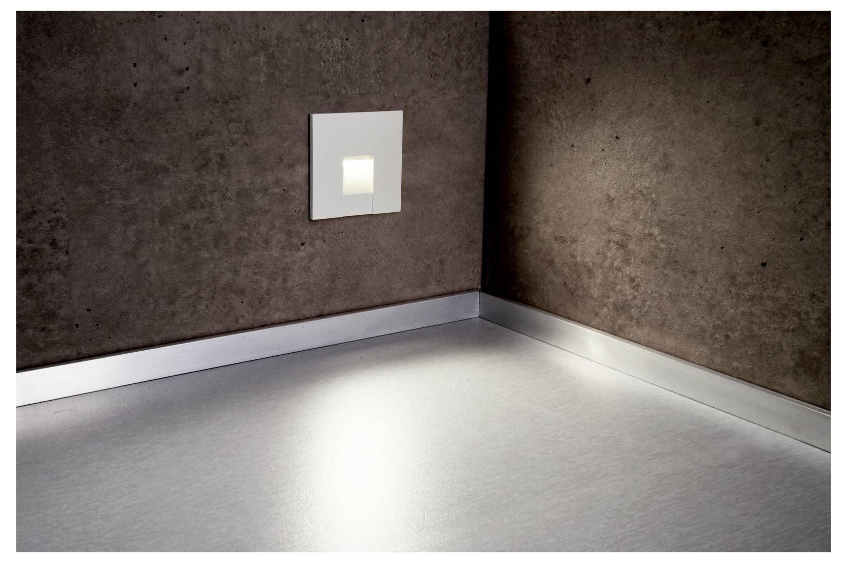 Klein vierkant wandlampje dat gloeit in een kale hoek van een kamer en een zacht lichtvlak op de vloer werpt.