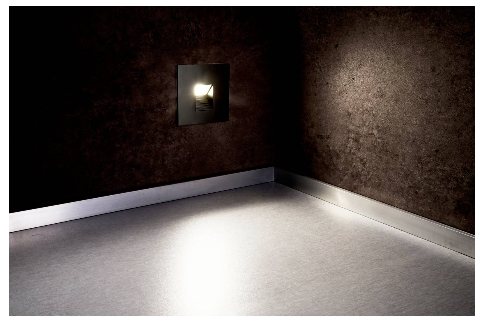 Lege kamer met donkere muren, een lichtgrijze vloer en een kleine opening in de muur die een heldere lichtstraal op de vloer werpt.